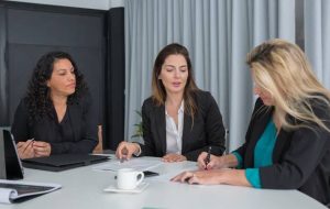 Tres mujeres conversando y firmando papeles en una reunión