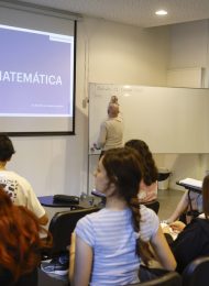 grupo de alumnos en clase de matemática, docente escribiendo en pizarra