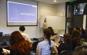 grupo de alumnos en clase de matemática, docente escribiendo en pizarra