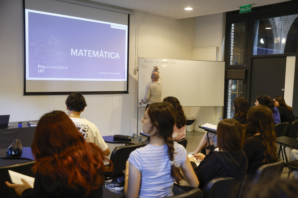 grupo de alumnos en clase de matemática, docente escribiendo en pizarra