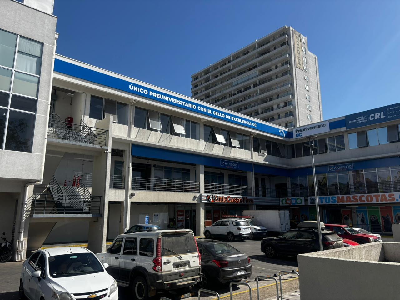 Fachada de la sede del Preuniversitario UC en maipú en edificio comercial, con letrero azul que dice 'Único preuniversitario con el sello de excelencia UC