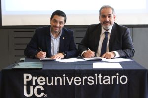 dos hombres firmando documentos sobre mesa con mantel preuniversitario uc